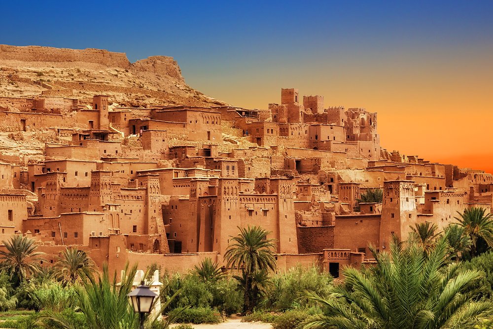 Sunset view of Aït Benhaddou, an ancient ksar near Ouarzazate, Morocco with traditional mudbrick architecture and palm trees