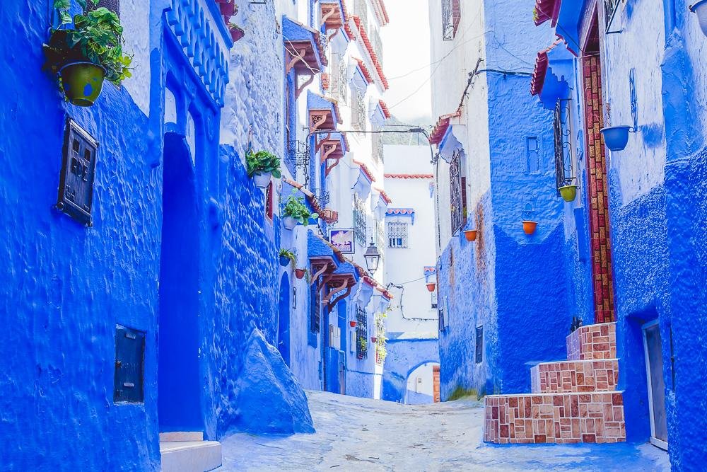 Bright blue alleyway in the medina of Chefchaouen, Morocco with flower pots and painted steps
