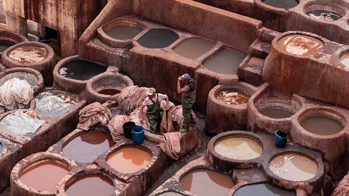 Workers at Chouara Tannery in Fes, Morocco dyeing leather in traditional stone vats filled with natural pigments