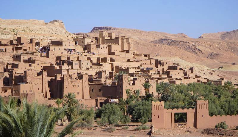 Aït Benhaddou, ancient fortified village in Morocco with traditional mudbrick architecture and palm trees under a clear blue sky