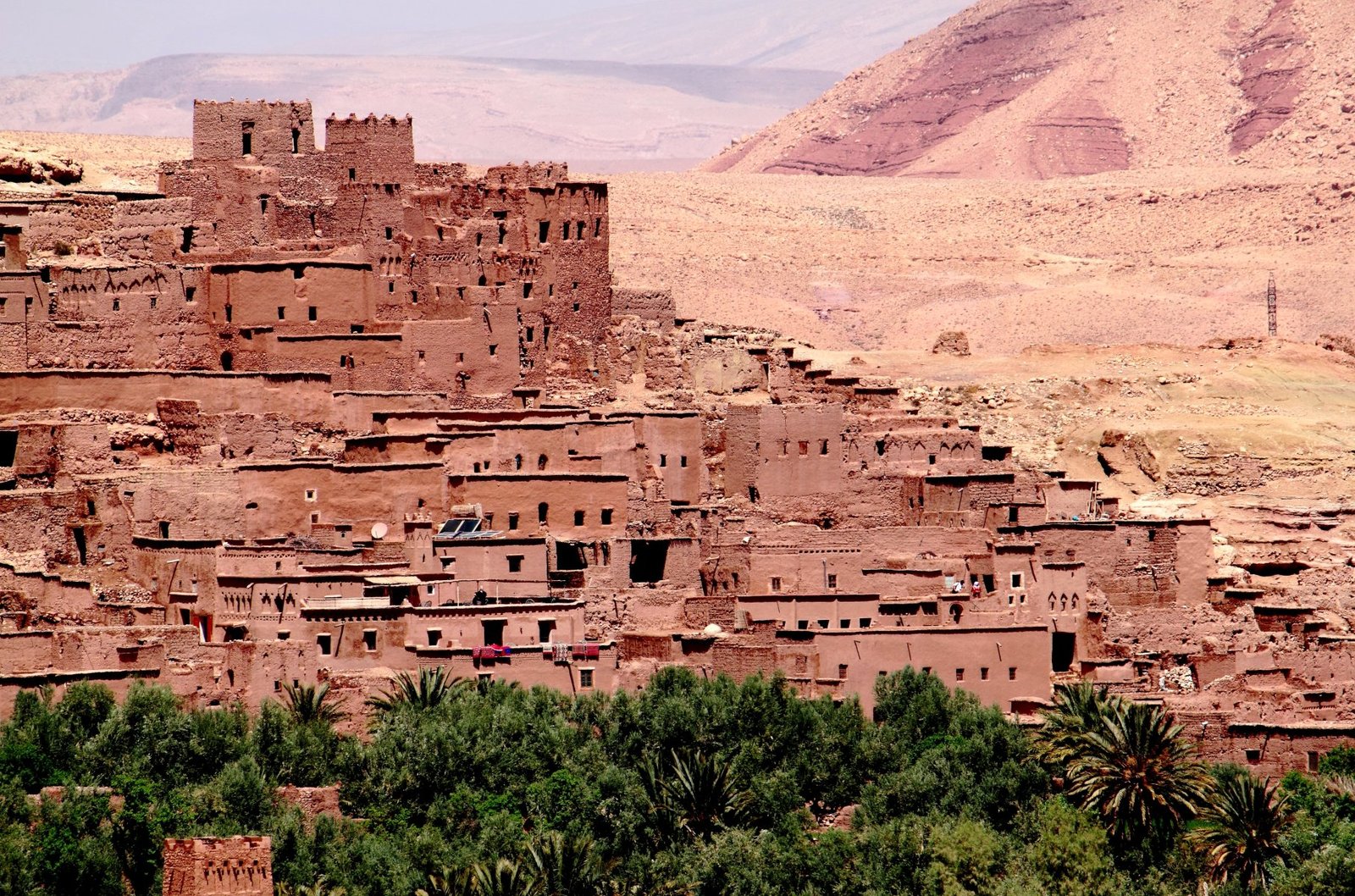 Sunset view of Aït Benhaddou, an ancient ksar near Ouarzazate, Morocco with traditional mudbrick architecture and palm trees