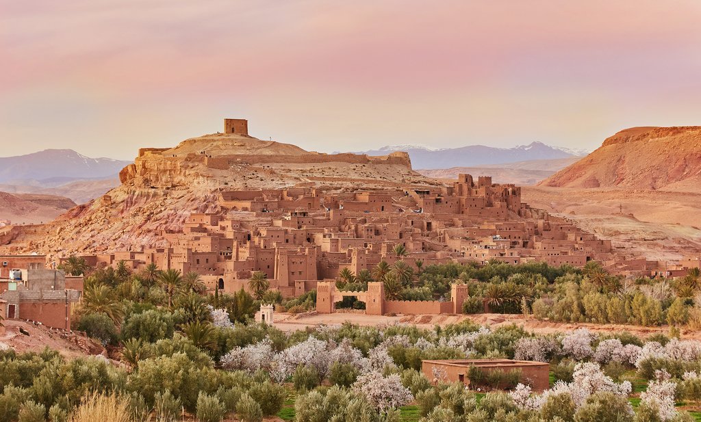 Panoramic view of Aït Benhaddou, an ancient ksar in Morocco, at sunset with surrounding desert hills