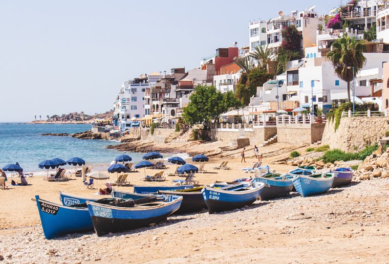 Traditional blue fishing boats on the beach in Asilah, Morocco with whitewashed buildings and palm trees in the background